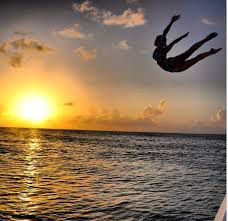 Woman in silhouette diving into water at sunset